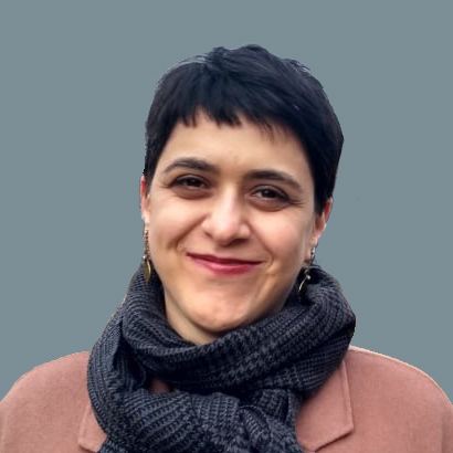 A picture of Sakine Bozorg. She smiles into the camera, has very short dark hair and wears a gray scarf.
